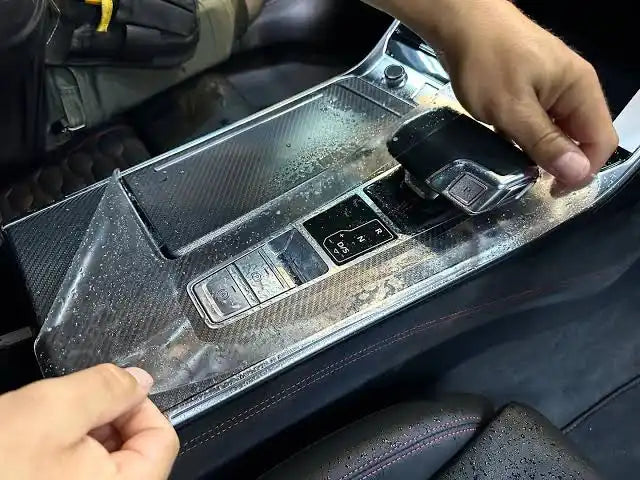 A clear protective film being applied to a car’s center console with carbon fiber trim.