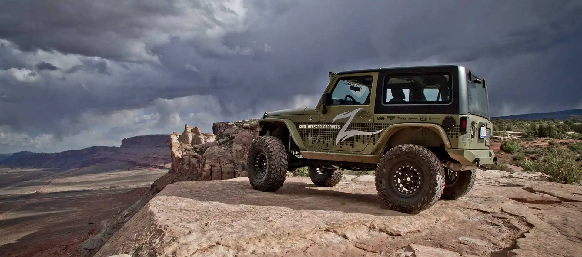 Olive green two-door Jeep Wrangler with a black hardtop and large off-road tires.